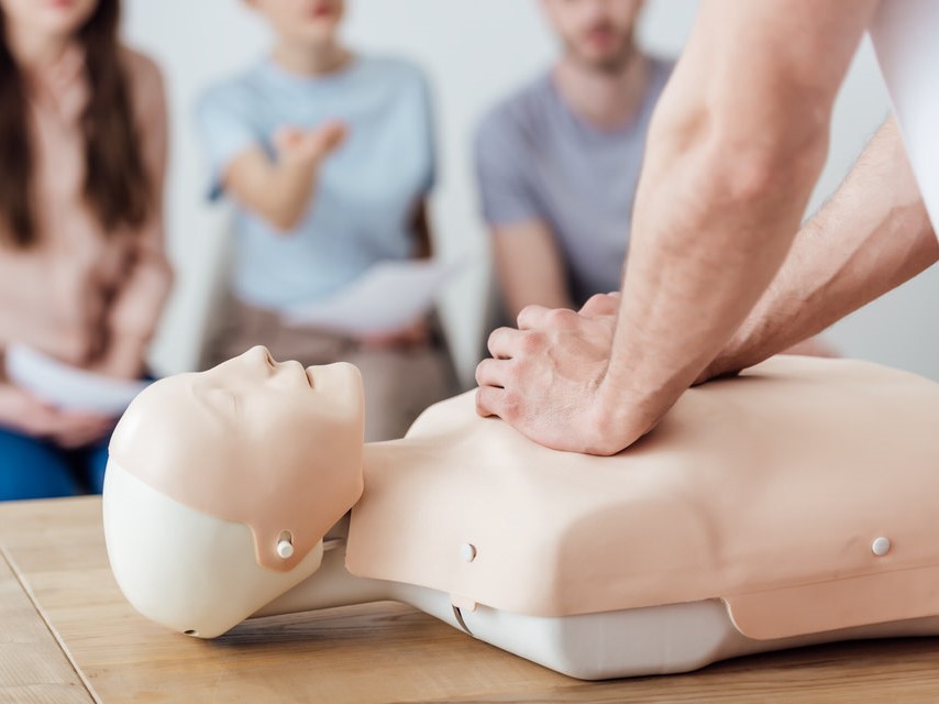 cropped view of instructor performing chest compression on dummy during cpr training class