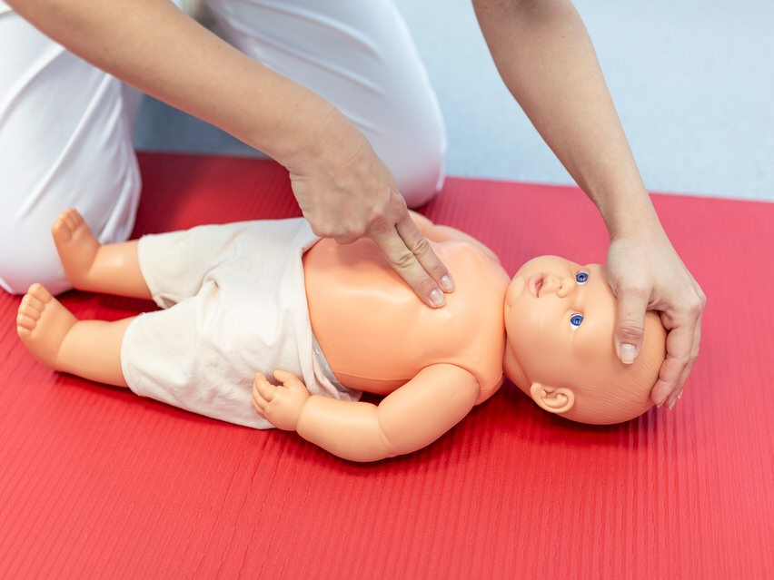 Woman performing CPR on baby training doll with one hand compression. First Aid Training - Cardiopulmonary resuscitation. First aid course on cpr dummy.